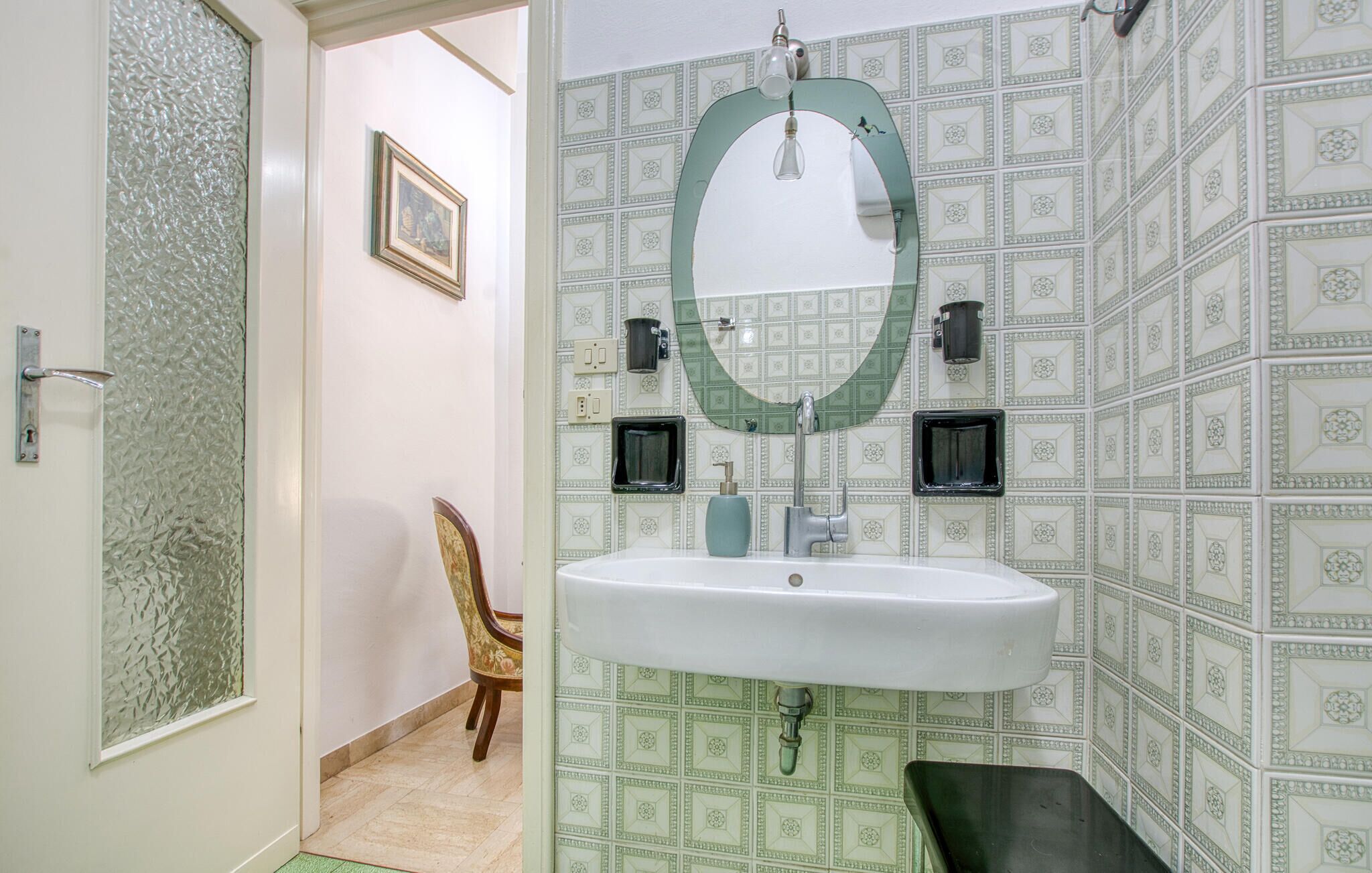 A bathroom with a white sink, a green mirror, and patterned tiles.