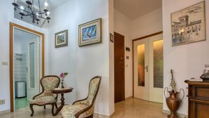 A hallway with two upholstered chairs, a small table, a vase with flowers, and a door with frosted glass panels.