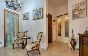 A hallway with two upholstered chairs, a small table, a vase with flowers, and a door with frosted glass panels.