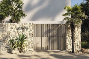 Ein verschlossener Eingang mit Steinmauer, Palmen und einem Schild, auf dem 'KOON I' steht.