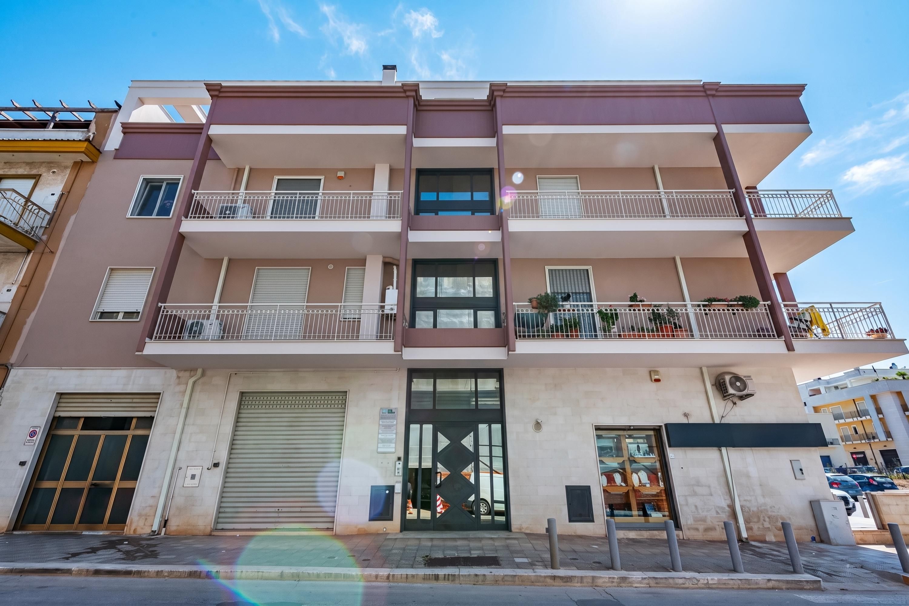 Un edificio residencial de varios pisos con balcones, garaje y una tienda en la planta baja.