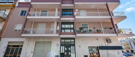 Un edificio residencial de varios pisos con balcones, garaje y una tienda en la planta baja.