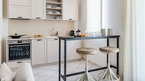 A modern kitchen with white cabinetry, a built-in oven, and a dining area with stools. - Welcome Suite (Conversano)