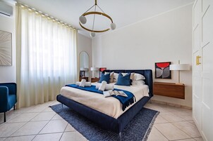 Quarto moderno com cama grande, mesa de cabeceira, luminária de teto e uma cadeira.