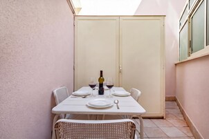 Uma pequena área de refeições ao ar livre com uma mesa posta para dois, incluindo pratos, talheres e uma garrafa de vinho.