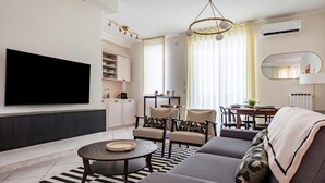 A modern living room with a flat-screen TV, a sofa, a dining area, and a kitchen. - Welcome Suite (Conversano)