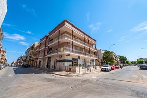 Um edifício residencial com várias andares, varandas, faixa de pedestres e carros estacionados.