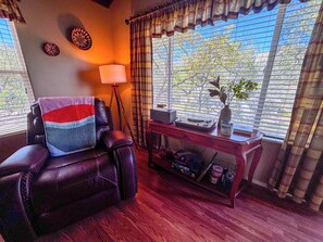 Ein Zimmer mit Ledersessel, Lampe, kleinem Tisch mit Vase und Fenster mit Jalousien.