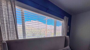 Une chambre à coucher avec un lit, une fenêtre avec des stores et une vue sur un paysage montagneux.