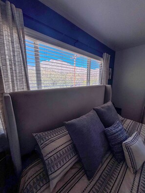Ein Schlafzimmer mit Bett, einem Fenster mit Jalousien und Blick auf eine Berglandschaft.