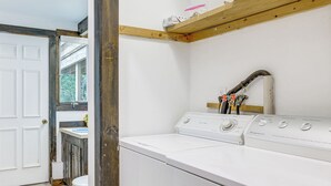 Ein Waschraum mit Waschmaschine und Trockner, einem Fenster und einer Tür zu einem anderen Raum.