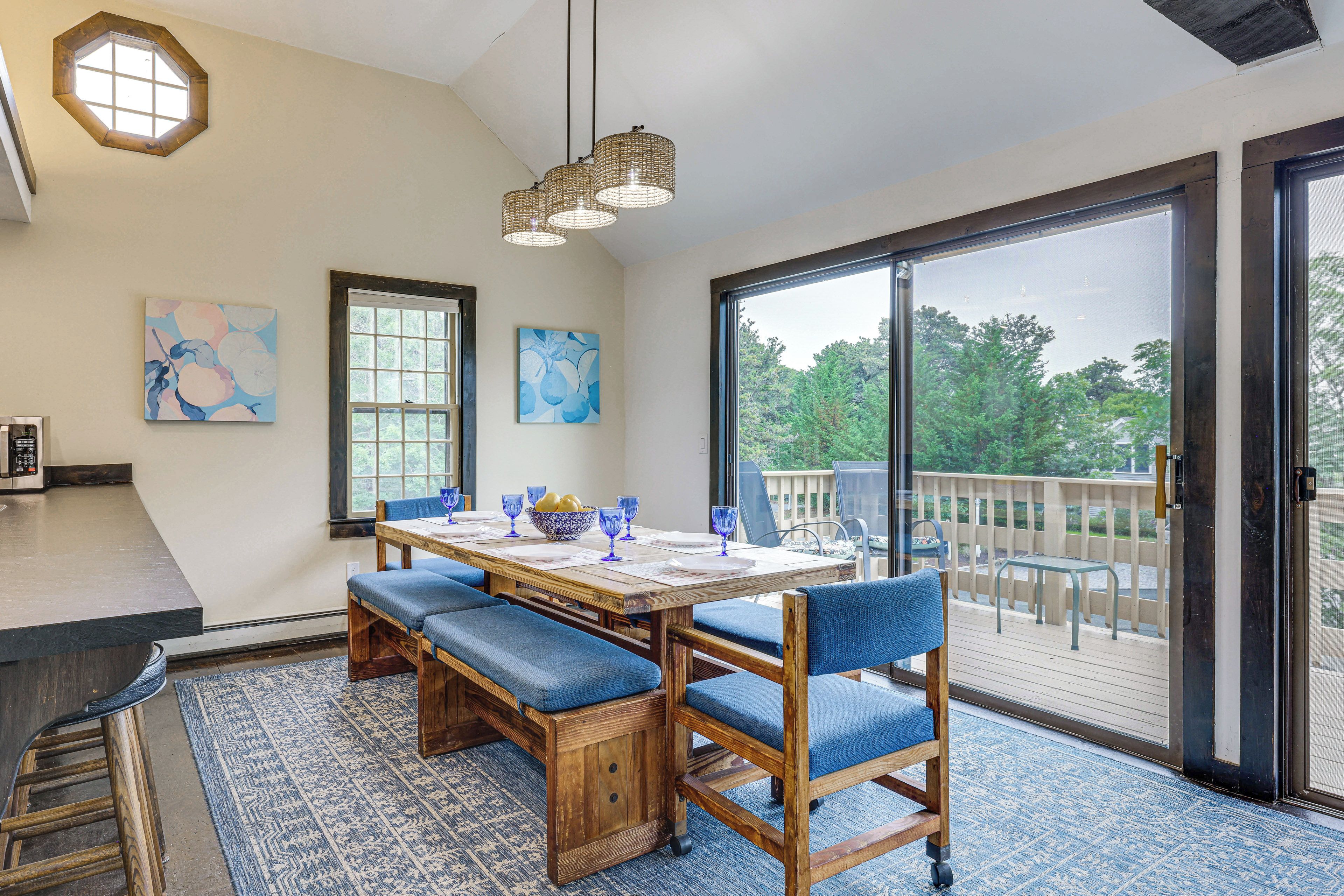 A dining area with a wooden table, blue cushioned chairs, and a view through a large sliding glass door to an outdoor deck.
