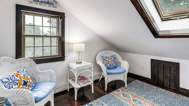 A room with two wicker chairs, a small table with a lamp, a window, and a patterned rug.