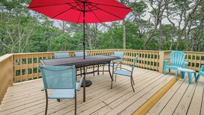Eine Terrasse mit Tisch, Stühlen und einem roten Sonnenschirm, sowie einem Holzaushandlung.