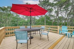 Eine Terrasse mit Tisch, Stühlen und einem roten Sonnenschirm, sowie einem Holzaushandlung.