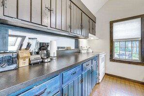 A kitchen with a dark countertop, blue cabinets, and a window with blinds. - Sea Breeze, Sunset Views! Family Escape Near Ocean (Wellfleet)