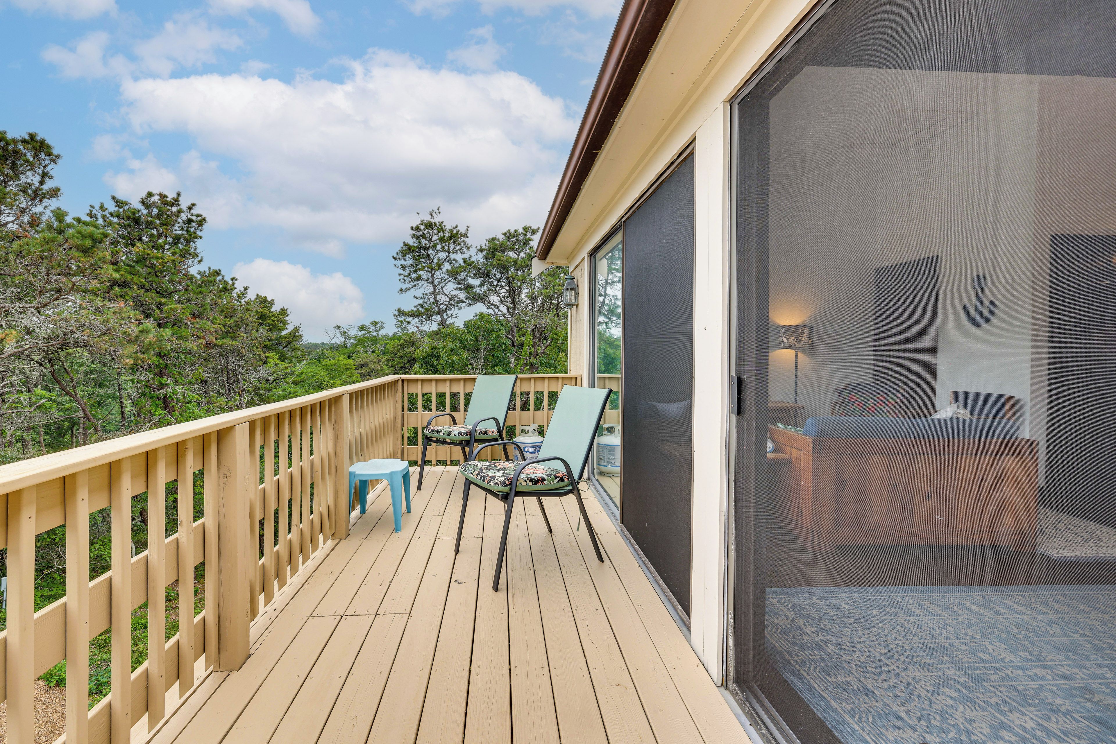 Una terraza con vistas al bosque circundante, una puerta corrediza que da a un dormitorio y mobiliario exterior.