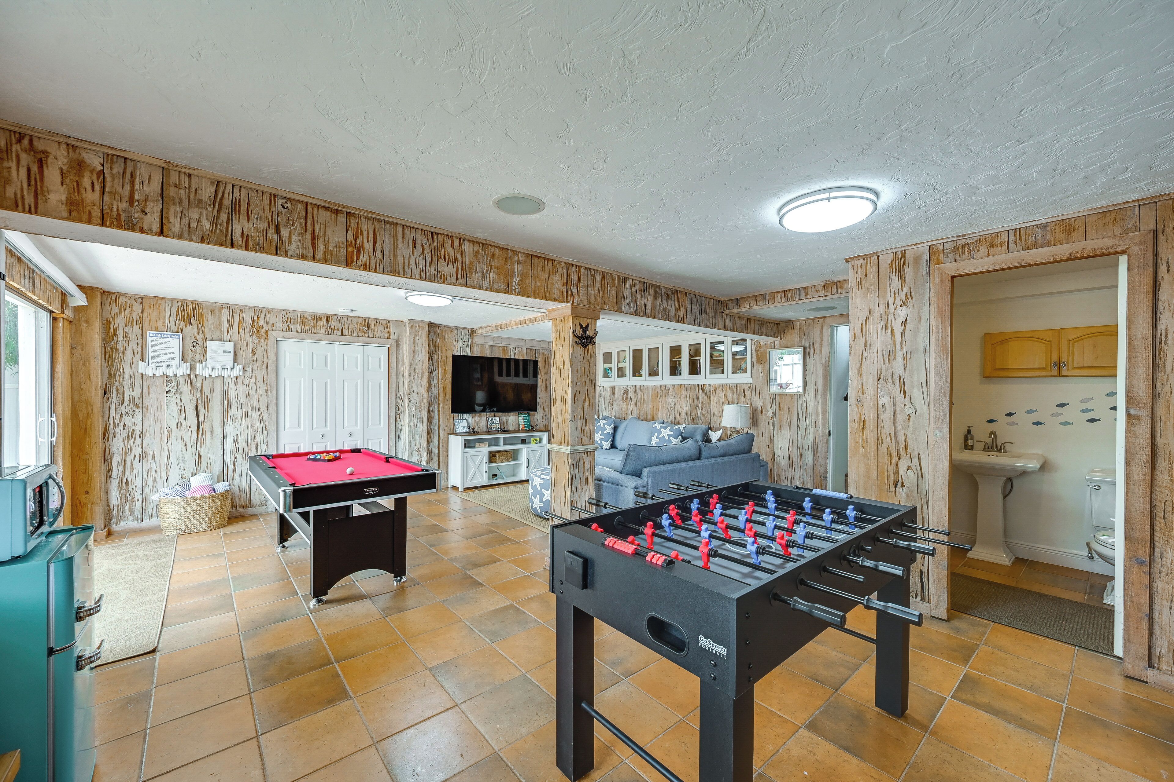 A room with a foosball table, a pool table, and a television.