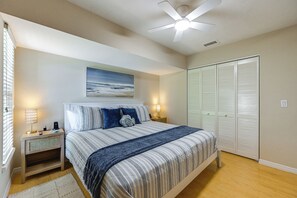 A bedroom with a bed, bedside lamps, a ceiling fan, a painting, and a wardrobe.