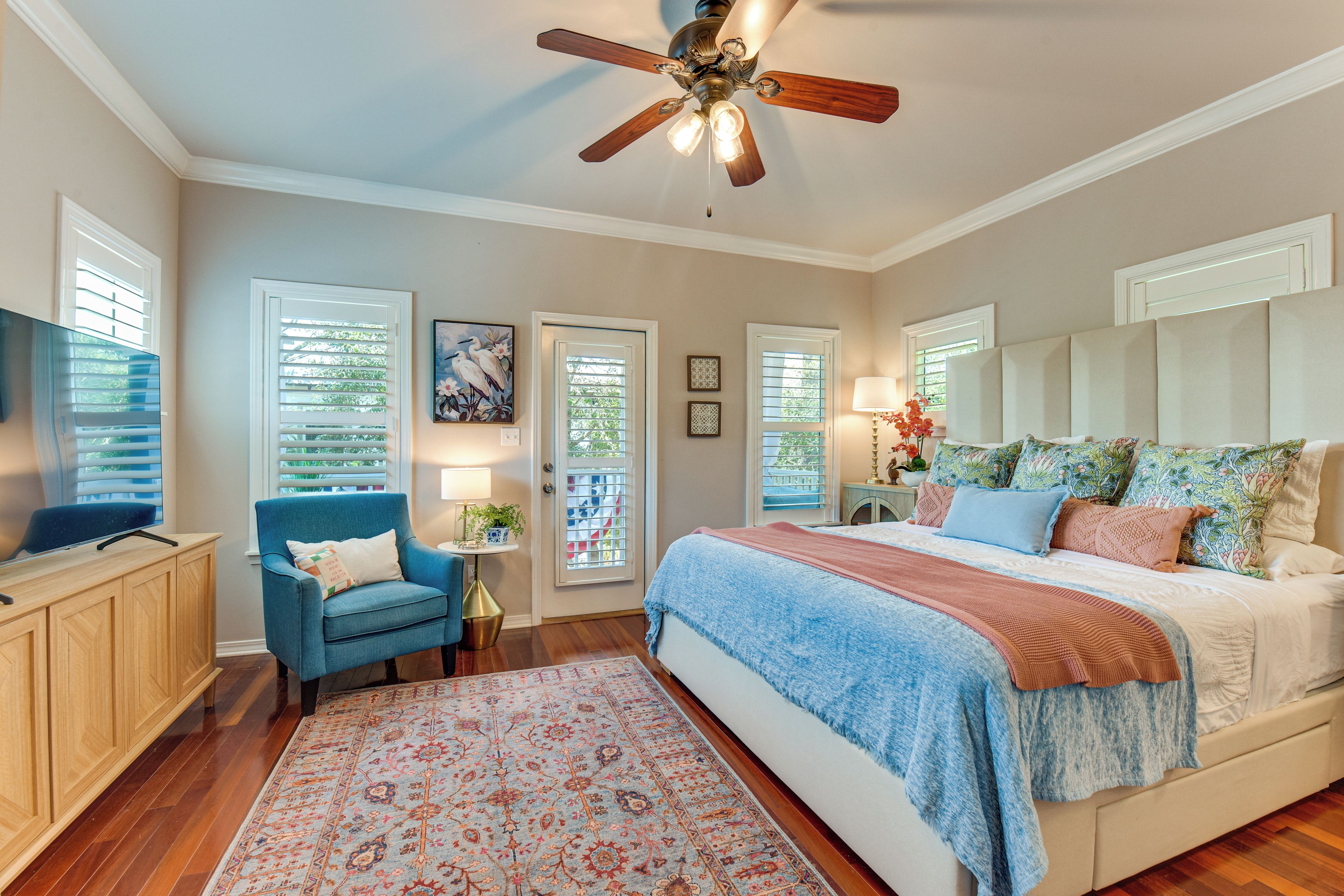 A bedroom with a bed, a desk, a chair, a ceiling fan, and a window with blinds.
