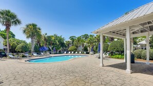 A swimming pool with hexagonal tiles, surrounded by lounge chairs and umbrellas, with palm trees and a covered seating area in the background. - Walkable 30A Beach House: 2 Community Pools, Bikes (Santa Rosa Beach)