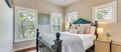 Un dormitorio con cama, mesitas de noche, ventilador de techo y ventanas con contraventanas.