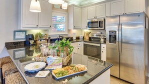 A modern kitchen with white cabinetry, stainless steel appliances, and a central island with a fruit platter. - Walkable 30A Beach House: 2 Community Pools, Bikes (Santa Rosa Beach)