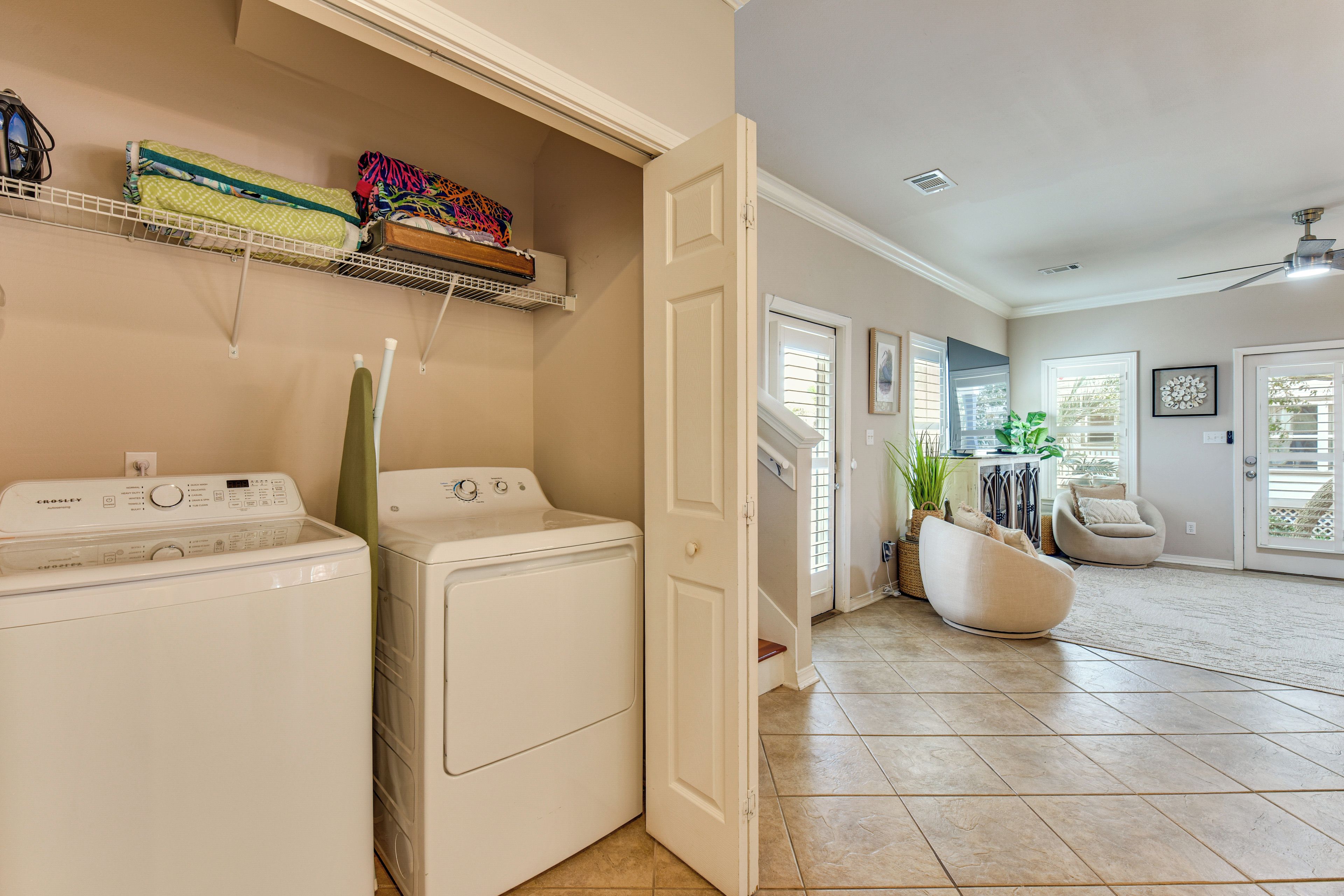 A laundry area with two front-loading washing machines, a drying rack, and a shelf with folded clothes.