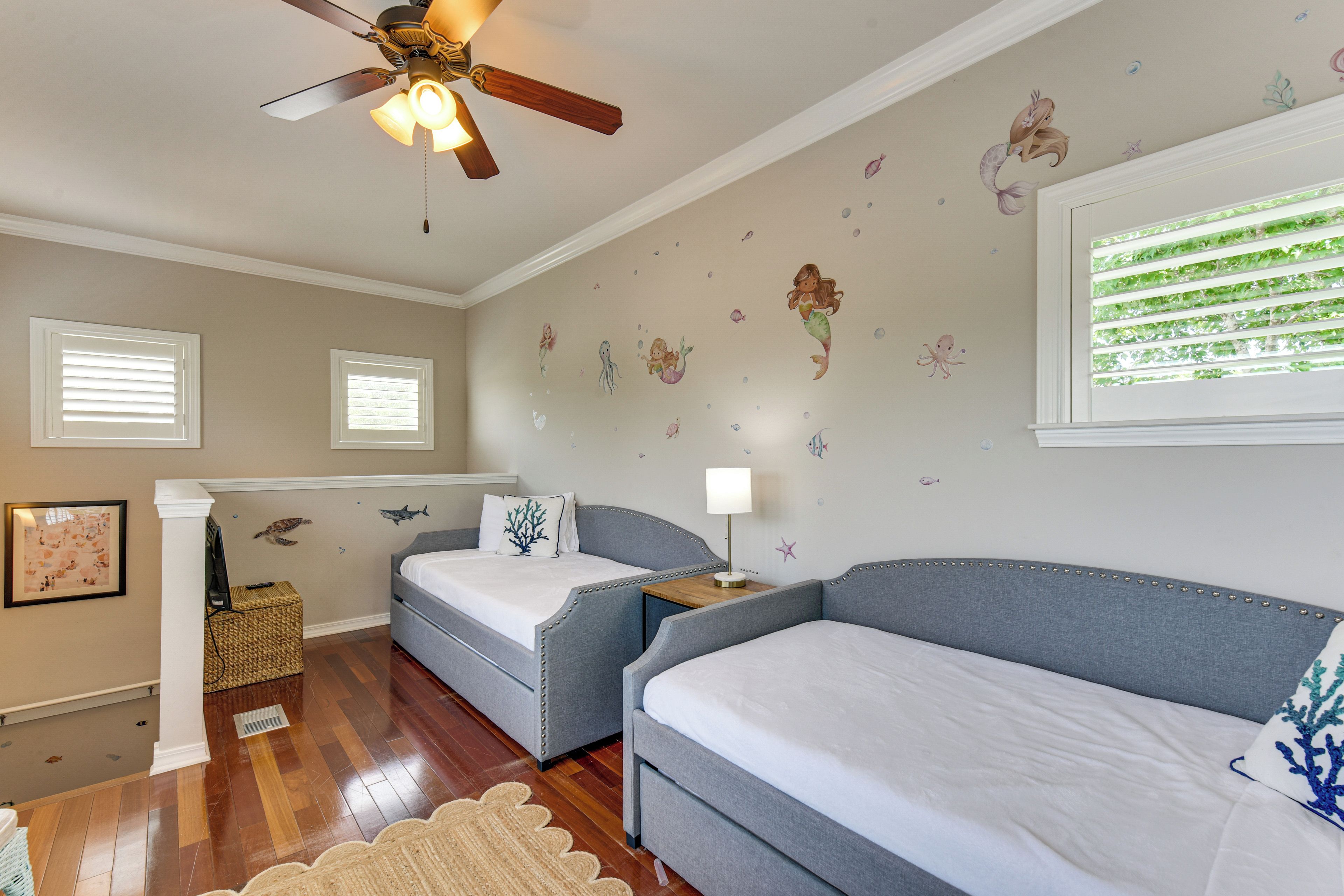 Une chambre à coucher comprenant un lit, un bureau, une chaise, un ventilateur de plafond et une fenêtre avec des stores.