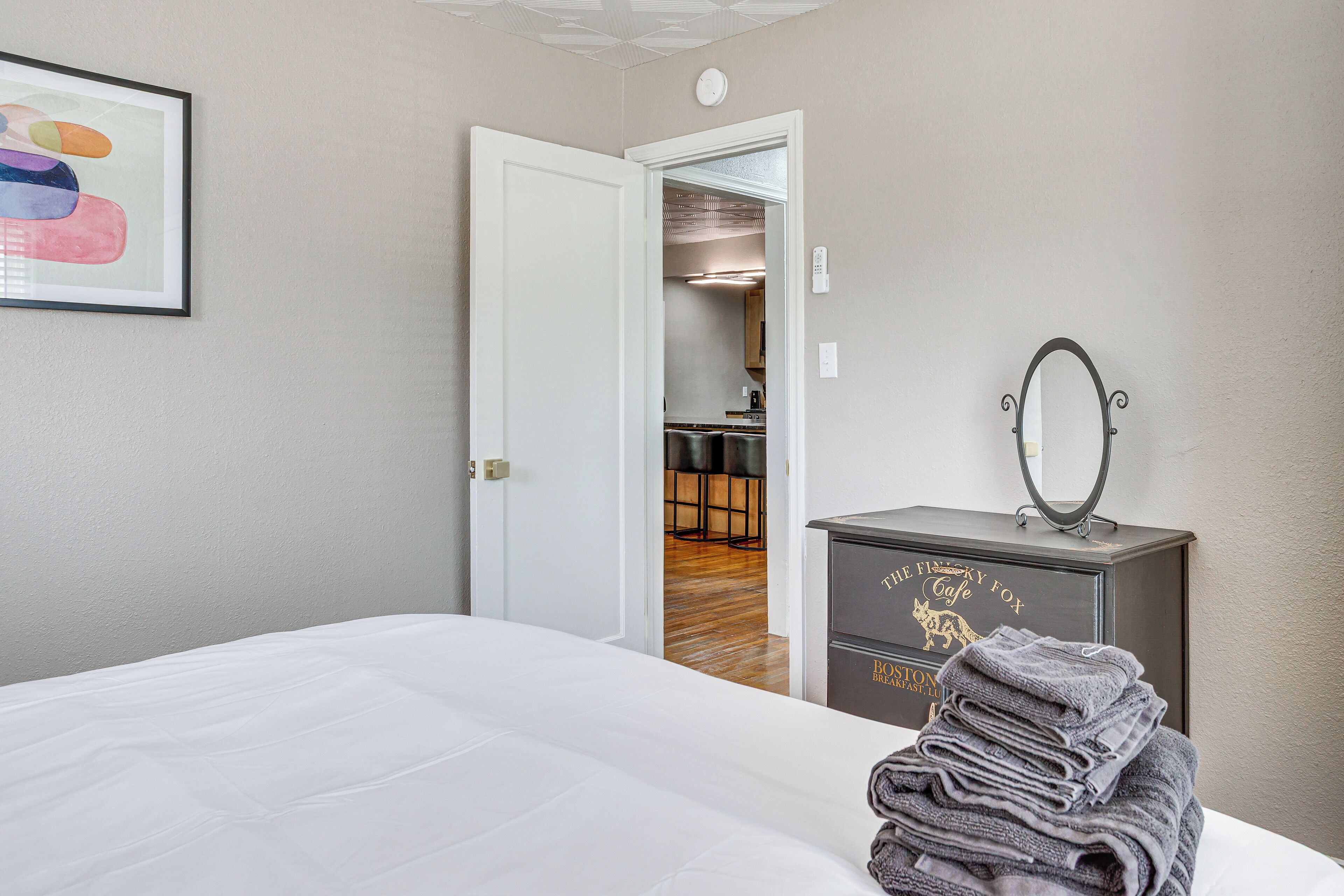 Una habitación de hotel con una cama bien hecha, un aparador con espejo y un cuadro en la pared.