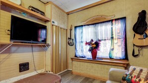 A living room with a television, a window with a guitar, and a bench.