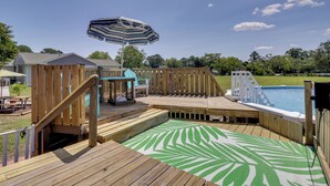 A wooden deck with a pool, a slide, and a green patterned area rug.