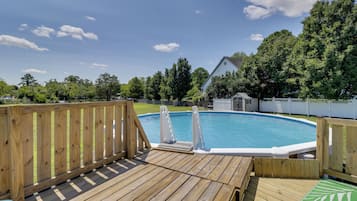 Una terrassa de fusta amb una piscina, envoltada per una tanca blanca i arbres.