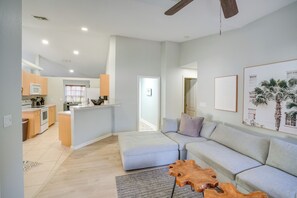 A modern living space with a kitchen, dining area, and a large grey sofa. - 4 Mi to River & Gardens! Quiet Port St Lucie Home (Port Saint Lucie)