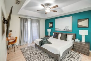 A modern bedroom with a bed, two bedside tables, a desk, a chair, a ceiling fan, and artwork on the walls. - 4 Mi to River & Gardens! Quiet Port St Lucie Home (Port Saint Lucie)