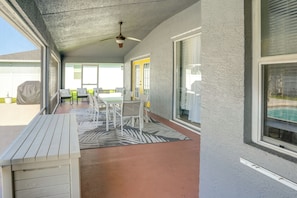 Ein überdachter Patio-Bereich mit Deckenventilator, einem Tisch mit Stühlen und Blick auf eine grüne Rasenfläche.