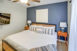 Ein Schlafzimmer mit einem Bett, zwei Nachttischen, einer Stehlampe, einem Deckenventilator, einer Wandleuchte und einem Fenster mit Vorhängen.