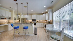 A modern kitchen with white cabinetry, a central island with stools, and a dining area with a glass table and wicker chairs. - 1 Block to Shore + Private Pool in Norfolk (Norfolk)