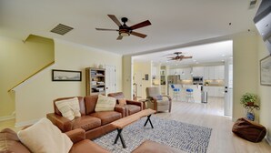 A spacious living room with a brown leather sofa, a wooden coffee table, and a patterned rug. There is a ceiling fan, a staircase, and a view into the kitchen area. - 1 Block to Shore + Private Pool in Norfolk (Norfolk)