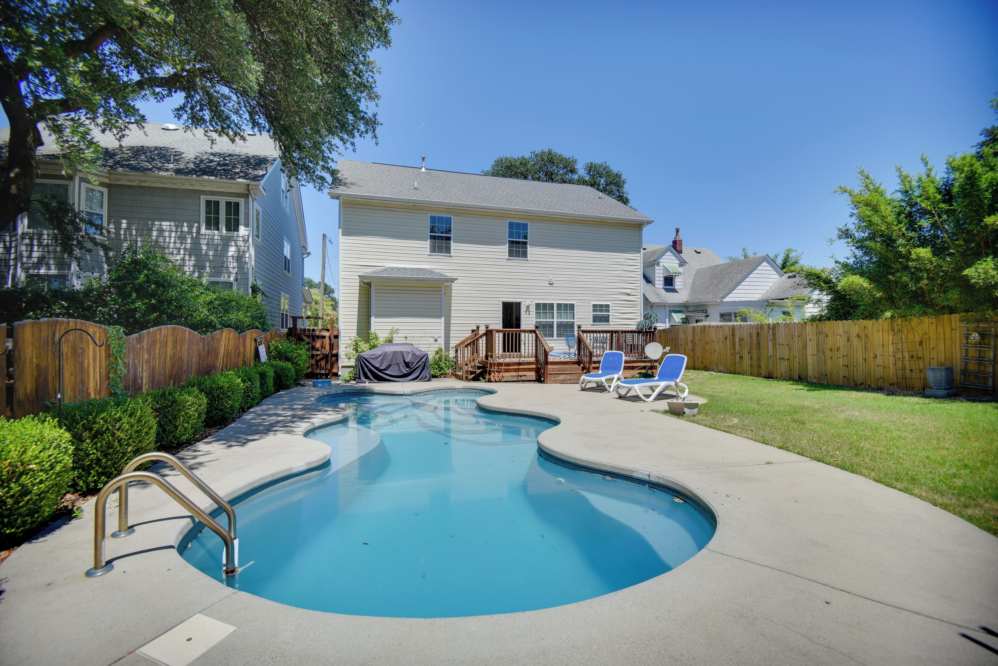 A residential swimming pool with a wooden deck, a covered grill, and a fenced backyard.