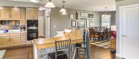 A kitchen with wooden cabinets, a built-in oven, and a bar area with stools.
