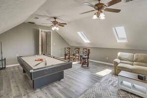 Una habitación amplia con mesa de billar, ventiladores de techo y sofá.
