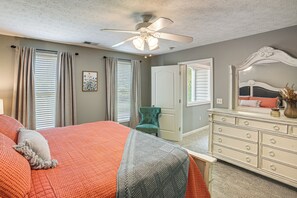 Um quarto com cama, cômoda, cadeira, ventilador de teto e uma porta.