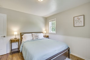 Um quarto com uma cama, duas mesinhas de cabeceira, uma janela e um quadro na parede.