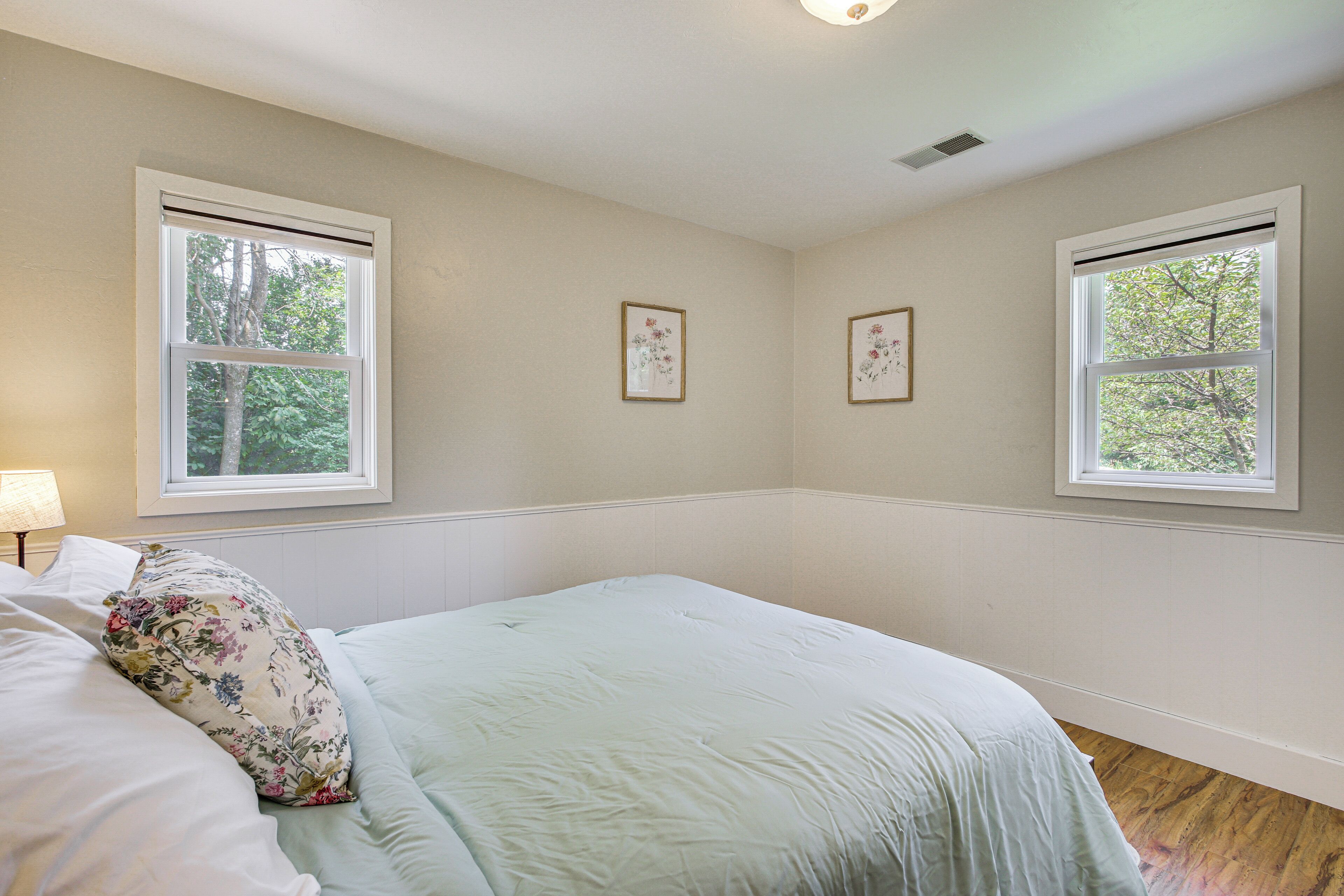Un dormitorio con una cama, dos ventanas y dos cuadros florales en la pared.