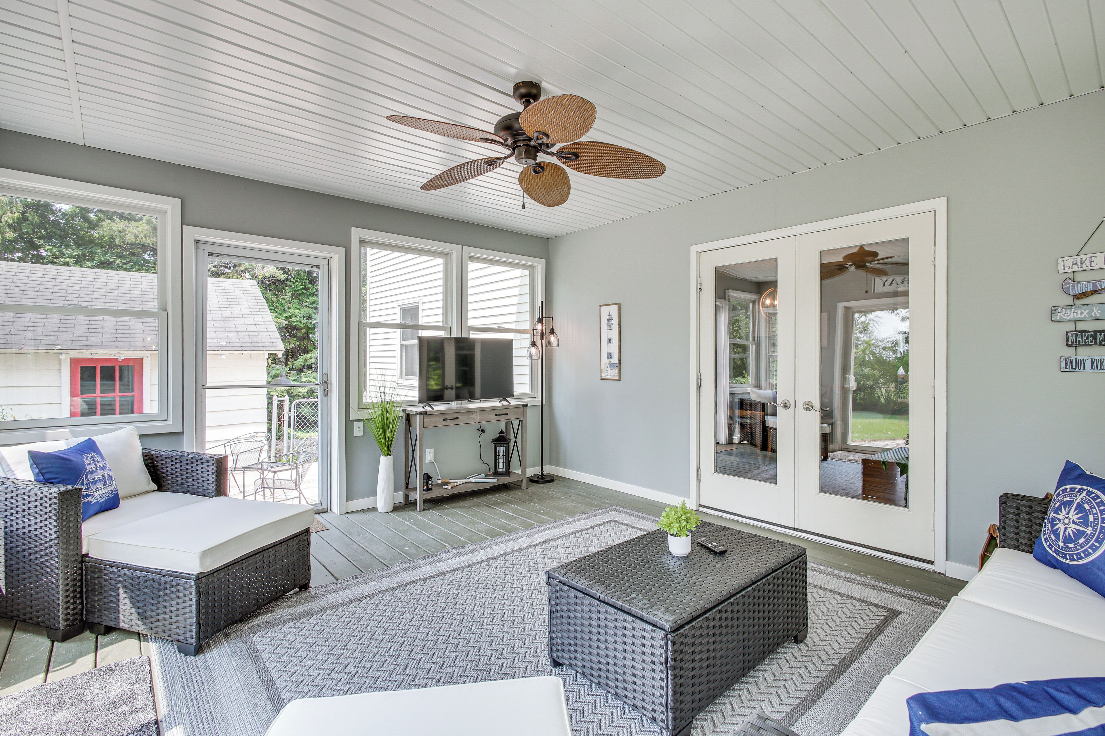A spacious living room with a ceiling fan, large windows, a television, and a dining area with outdoor seating.
