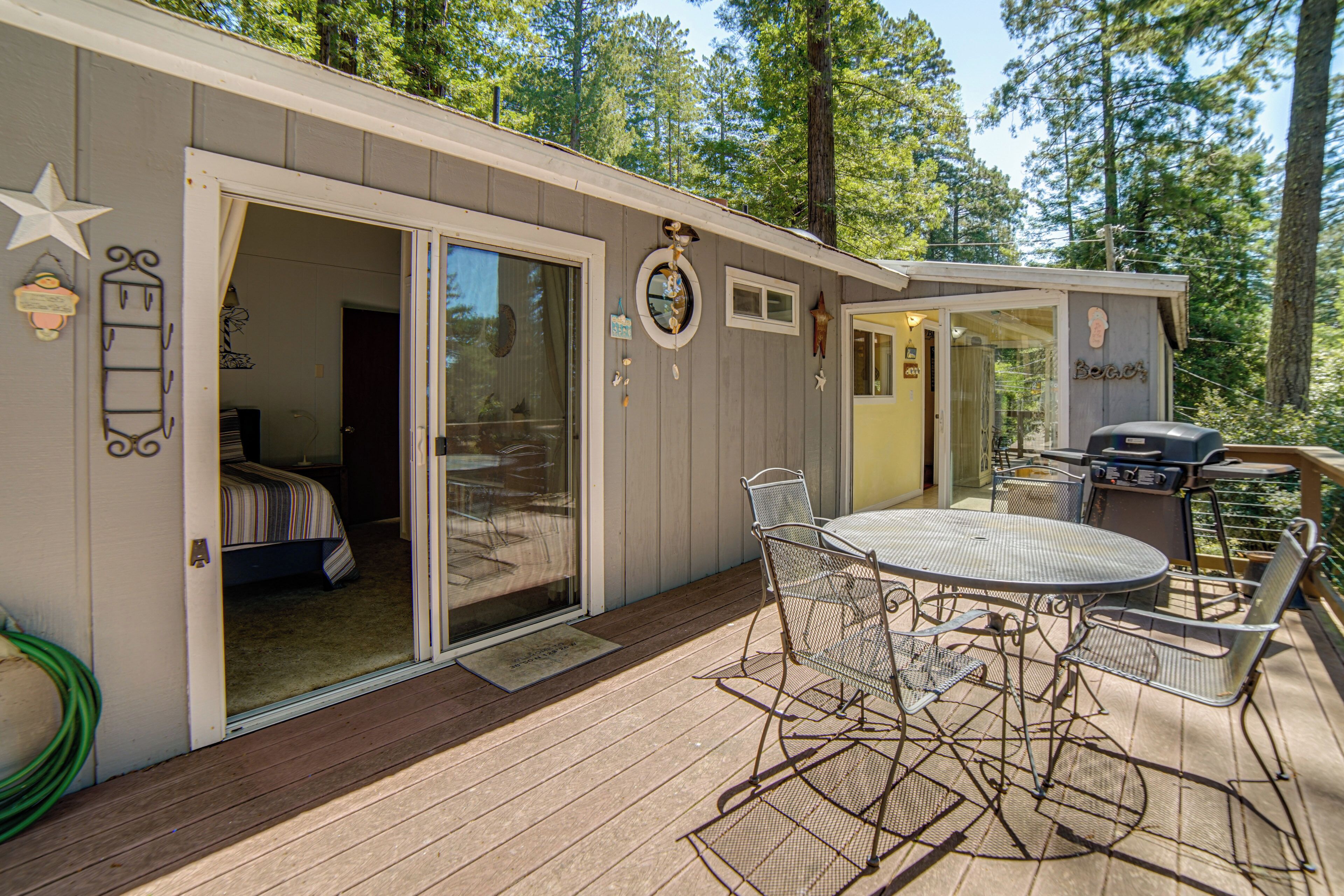 A cabin with a patio area featuring a round table and chairs, a grill, and a sliding glass door leading to a bedroom.