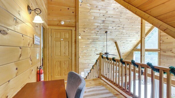A wooden interior with a staircase leading to a balcony, a fire extinguisher, and a door with a sign. - Ellijay Cabin Hot Tub, Mtn Views & Game Room (Ellijay)