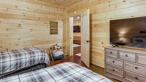 A wooden cabin room with two beds, a dresser, and a television. - Ellijay Cabin Hot Tub, Mtn Views & Game Room (Ellijay)