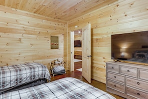 Ein Zimmer in einer Holzhütte mit zwei Betten, einem Schminktisch und einem Fernseher.